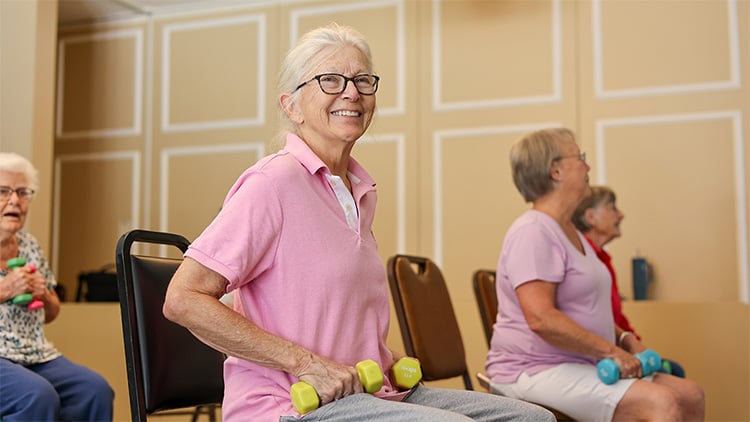 Healthy active senior woman lifting light weights in fitness class