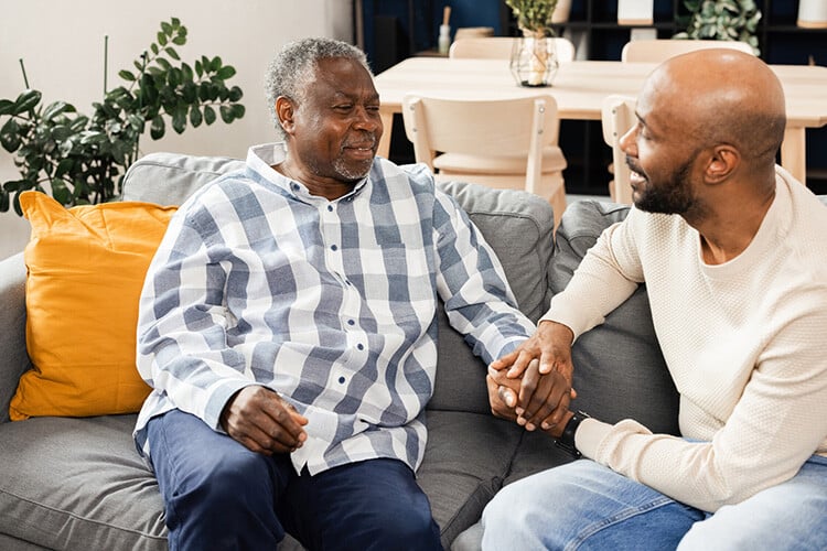 Senior man and adult son holding hands and talking 