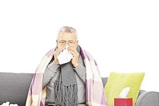 Senior man sitting on sofa with tissues looking ill