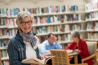 A healthy senior woman holding a book in a senior living library