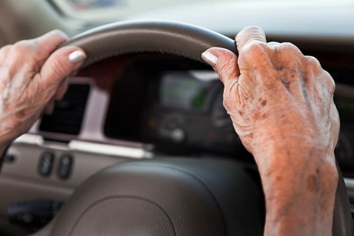 senior person's hands on car steering wheel