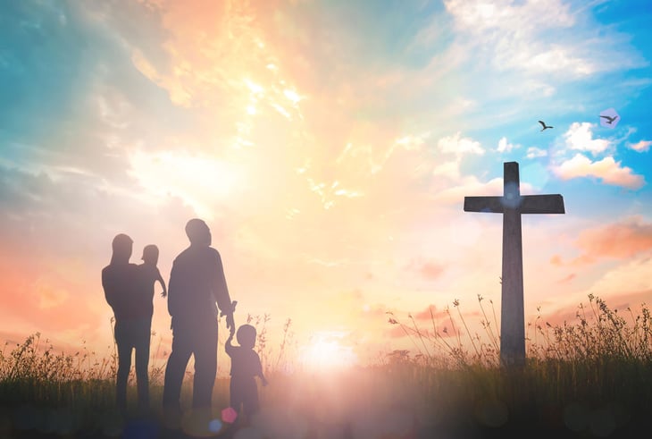 family and cross silhouette in front of sunset