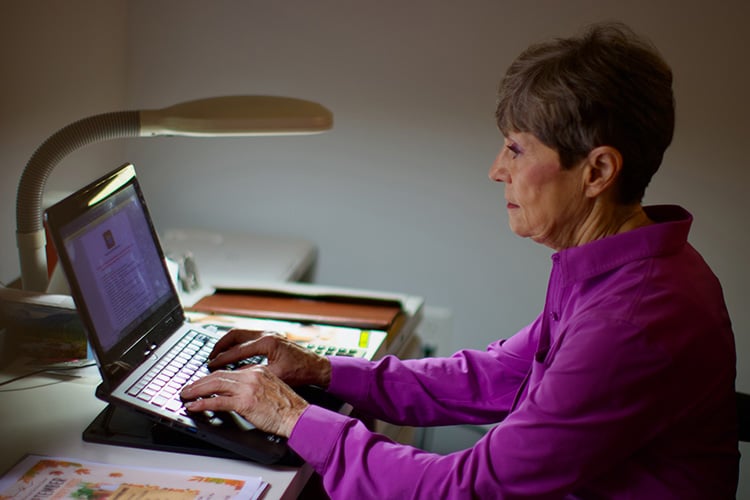 Creative senior writing at a laptop at a desk